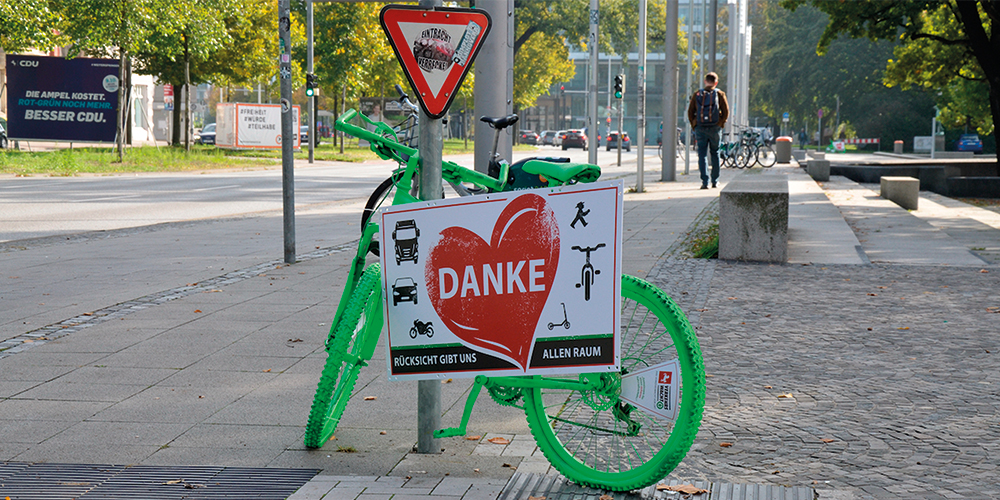 Grünes Fahrrad an einer Laterne mit Schild: "Danke" in einem Herz mit Aufschrift: Rücksicht gibt uns allen Raum